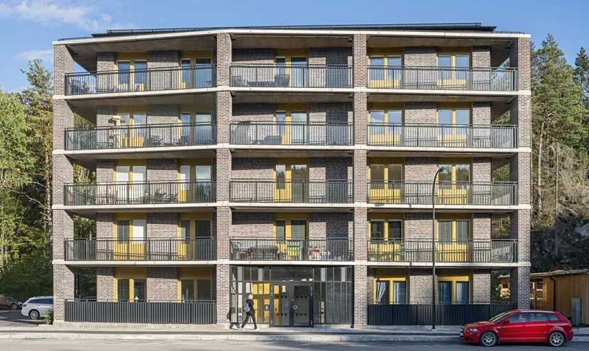 En solig sommarkväll framför föreningens ena hus, Gaffelseglet 39 som har fem våningar och en tegelfasad med gula detaljer. Den gröna skogsdungen syns i bakgrunden.